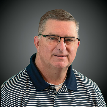 Morris Hartley, a man with short gray hair and glasses, wears a navy and white striped polo shirt in front of a plain dark background.