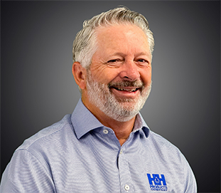 A smiling older man with gray hair and beard, Wayne Zeigler wears a light blue collared shirt with an H&H logo, posing in front of a dark gradient background.